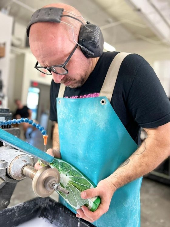 A person in black ear protectors working on a large glass lime wedge.